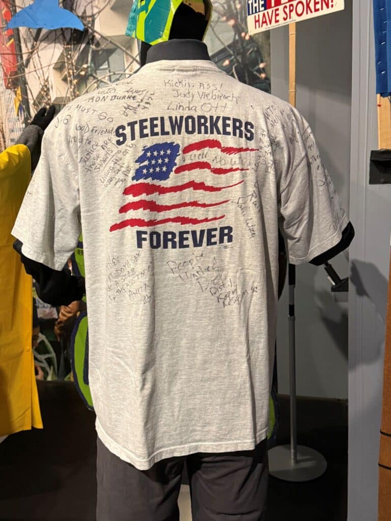 A Steelworkers t-shirt with a stylized American flag and "Steelworkers Forever" in text. The shirt is hand signed by many people who attended the 1999 "Battle in Seattle" protesting the World Trade Organization.